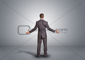 Businessman standing in an empty gray room. Rear view