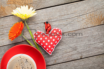 Cup of coffee, heart toy and gerbera flowers on wooden table