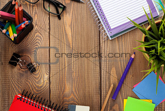 Office table with notepad, colorful pencils, supplies and flower
