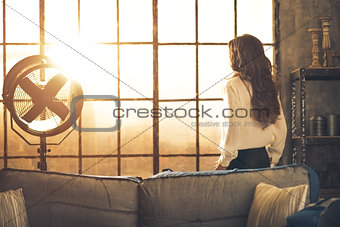 Young woman looking in window in loft apartment. rear view