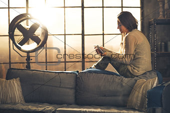 Young woman sitting in loft apartment and using tablet pc