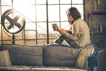 Happy young woman sitting in loft apartment and using tablet pc