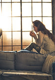 Young woman enjoying cup of hot beverage in loft apartment