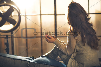 Young woman enjoying cup of hot beverage in loft apartment. rear