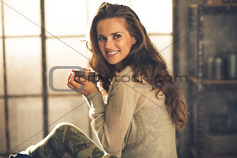 Portrait of happy young woman with cup of coffee in loft apartme