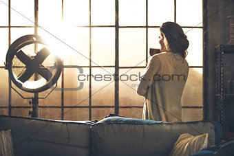 Young woman enjoying cup of coffee in loft apartment. rear view