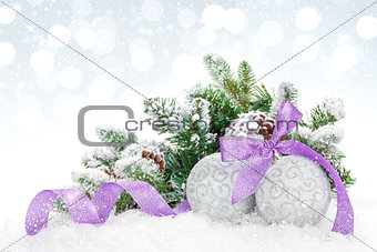 Christmas baubles and purple ribbon over snow bokeh background
