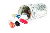 colorful pills in front of rolled up dollars on white background