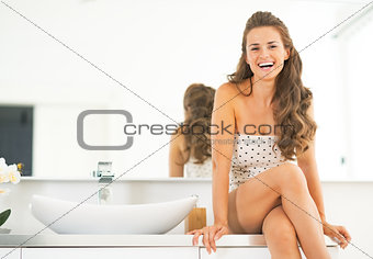 Happy young woman sitting in bathroom