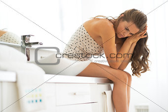Frustrated young woman sitting in bathroom