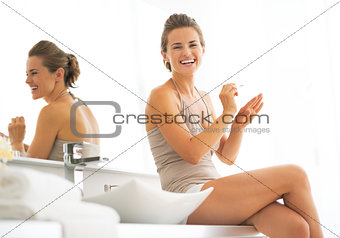 Smiling young woman applying nail polish in bathroom