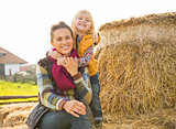 Portrait of smiling mother and child sitting on haystack