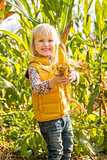 Portrait of smiling child showing corn while in cornfield