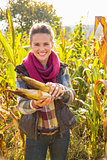 Happy young woman holding corn while standing in cornfield