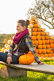 Smiling young woman sitting with pumpkin in front of pumpkin pir