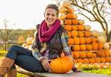 Portrait of happy young woman sitting with pumpkin in front of p