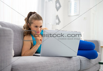 Young woman laying on sofa with laptop