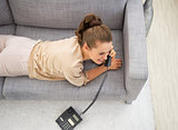 Young woman laying on divan in living room and talking phone