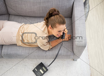 Young woman laying on divan in living room and talking phone