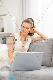 Thoughtful young housewife with laptop in living room