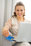 Portrait of happy young housewife with laptop holding credit car