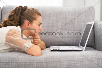 Young woman laying on couch and using laptop