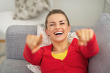 Happy young woman laying on couch and pointing in camera