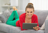 Smiling young woman laying on couch with tablet pc
