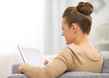 Young woman sitting on sofa and using tablet pc. rear view