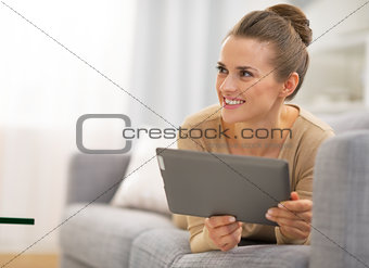 Thoughtful young woman laying on couch and using tablet pc