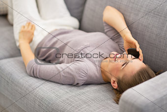 Happy young woman laying on couch and talking cell phone