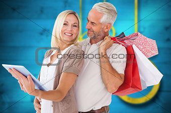 Composite image of happy couple with shopping bags and tablet pc