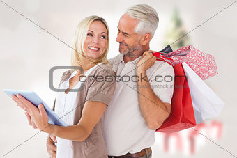 Composite image of happy couple with shopping bags and tablet pc