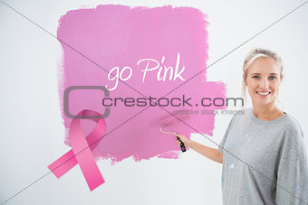 Composite image of happy young woman painting her wall pink
