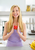 Portrait of smiling young woman with apple in kitchen