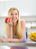 Portrait of happy young woman with apple in kitchen