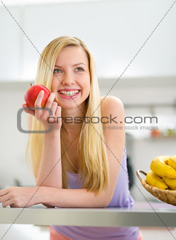 Portrait of happy young woman with apple in kitchen