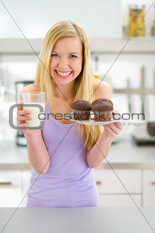 Portrait of happy teenager girl with muffin and milk in kitchen