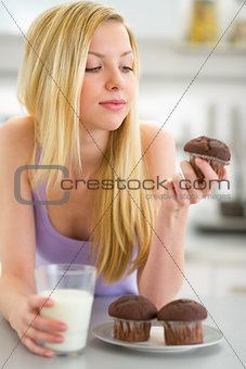 Teenager girl eating muffin with milk in kitchen