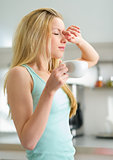 Sleepy young woman with cup of coffee in kitchen