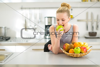 Portrait of young woman eating apple in kitchen