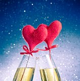 champagne flutes with golden bubbles and red velvet hearts make cheers on blue bokeh background