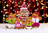 Gingerbread cookie family in front of christmas tree