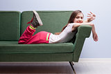 little girl waving at the camera lying on a green sofa