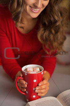 Closeup on young woman with cup of hot chocolate and book