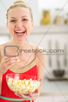 Portrait of happy young woman eating popcorn in kitchen
