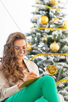Smiling young woman writing in christmas postcard near christmas