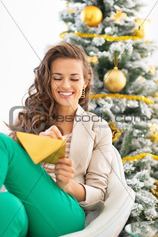 Happy young woman writing christmas letter near christmas tree