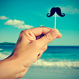 man hand with a fake moustache on the beach, with a filter effec