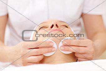 Cosmetician cleaning face using cotton pads